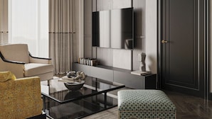 A modern living room with a sofa, a coffee table, a patterned ottoman, a flat-screen TV mounted on a wall, and a door. - Baku Resort & Spa (Cholpon-Ata)