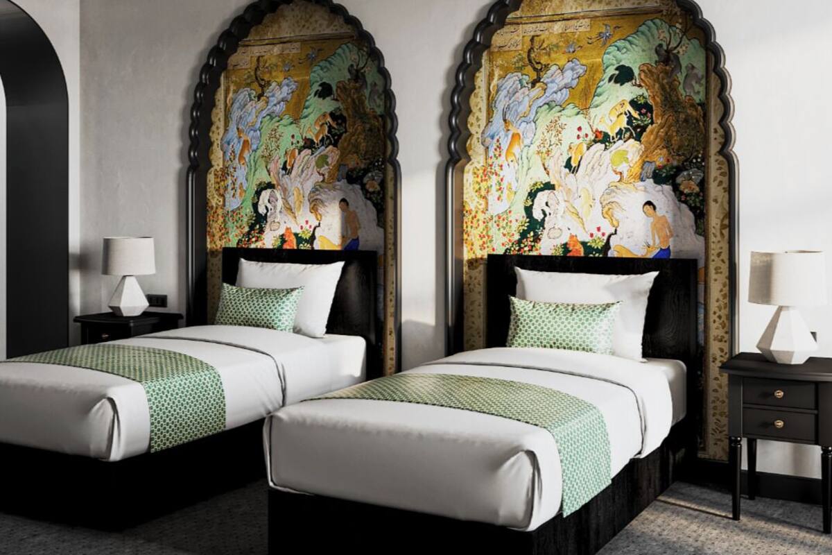 Quarto de hotel com duas camas, um mural grande na parede, uma luminária de teto preta e uma pequena mesa com abajur.