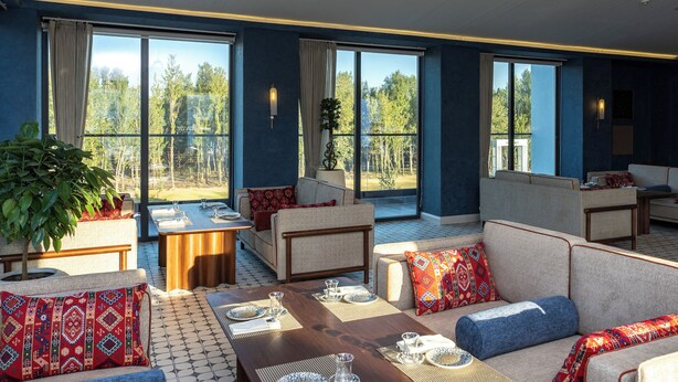 Amplia sala de estar con diversas opciones de asientos, una mesa de comedor dispuesta para una comida y ventanas grandes con vistas al exterior.