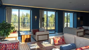 A spacious lounge area with multiple seating options, a dining table set for a meal, and large windows offering a view of the outdoors.