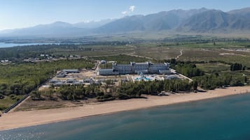 Un complejo turístico frente al mar con varias construcciones, una playa y montañas al fondo.