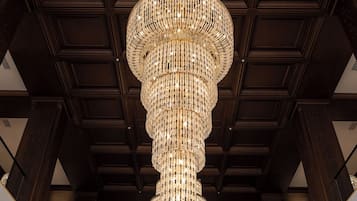 Un magnifique lustre trône dans un vaste hall aux hauts plafonds et aux murs lambrissés.