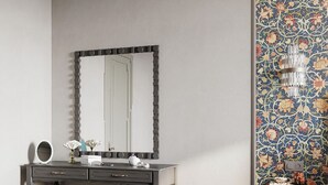 Una habitación con tocador, espejo, taburete, una mesita con un cartel y pared con diseño.