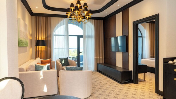 A hotel room with a sofa set, a flat-screen TV, a desk, and a chandelier. - Baku Resort & Spa (Cholpon-Ata)