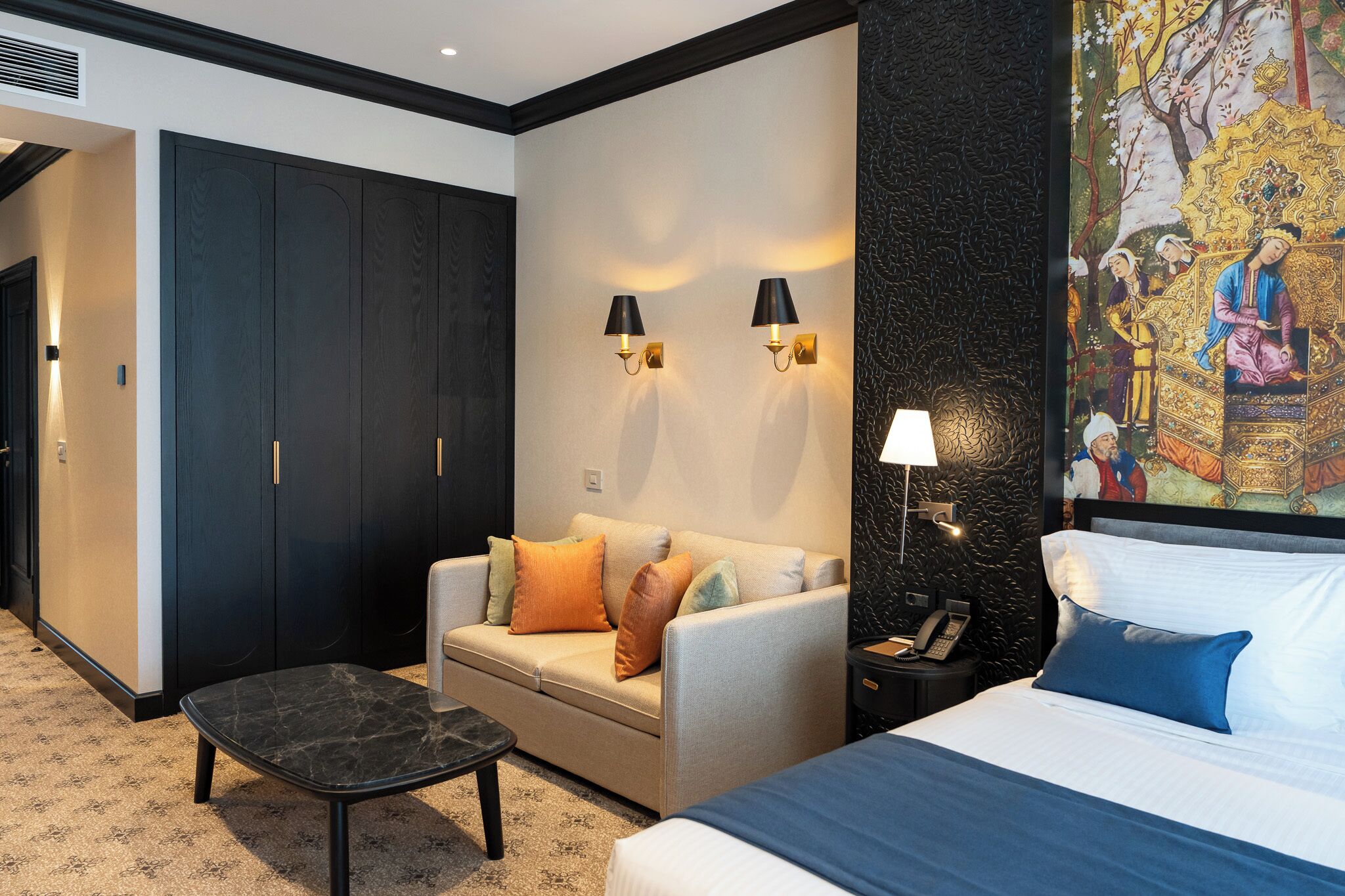 A hotel room with a bed, a sofa, a small table, and a painting on the wall.
