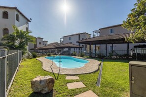 A swimming pool surrounded by a paved deck, a stone pathway, and a fenced area with a palm tree. - Charming 2-bedroom Apartment With Ocean and Mountain Views (Plettenberg Bay)