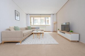Una sala de estar moderna con un sofá, una mesa de centro, un televisor sobre un mueble bajo y una ventana con persianas.