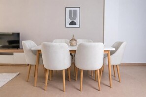 Ein Essbereich mit einem weißen Tisch und Stühlen, einem gerahmten Kunstwerk an der Wand und einem Fernseher links.