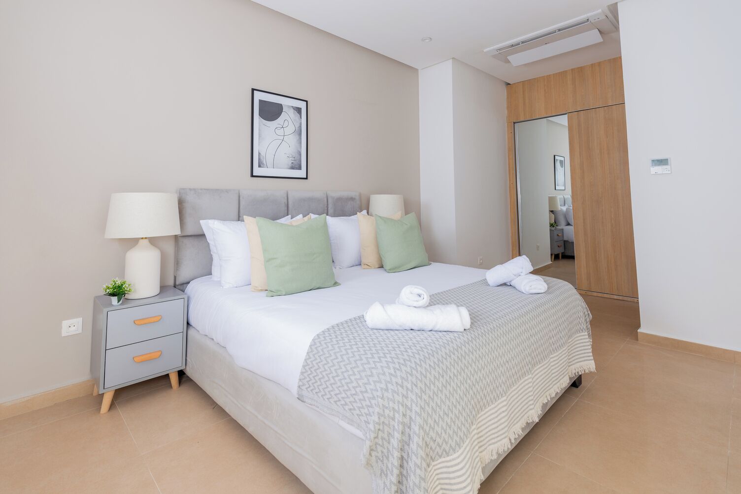 A neatly made bed with pillows and a blanket, a bedside table with a lamp, and a framed picture on the wall.