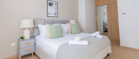 A neatly made bed with pillows and a blanket, a bedside table with a lamp, and a framed picture on the wall.