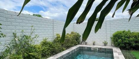 A rectangular swimming pool with a tiled edge, surrounded by a low wall and greenery.