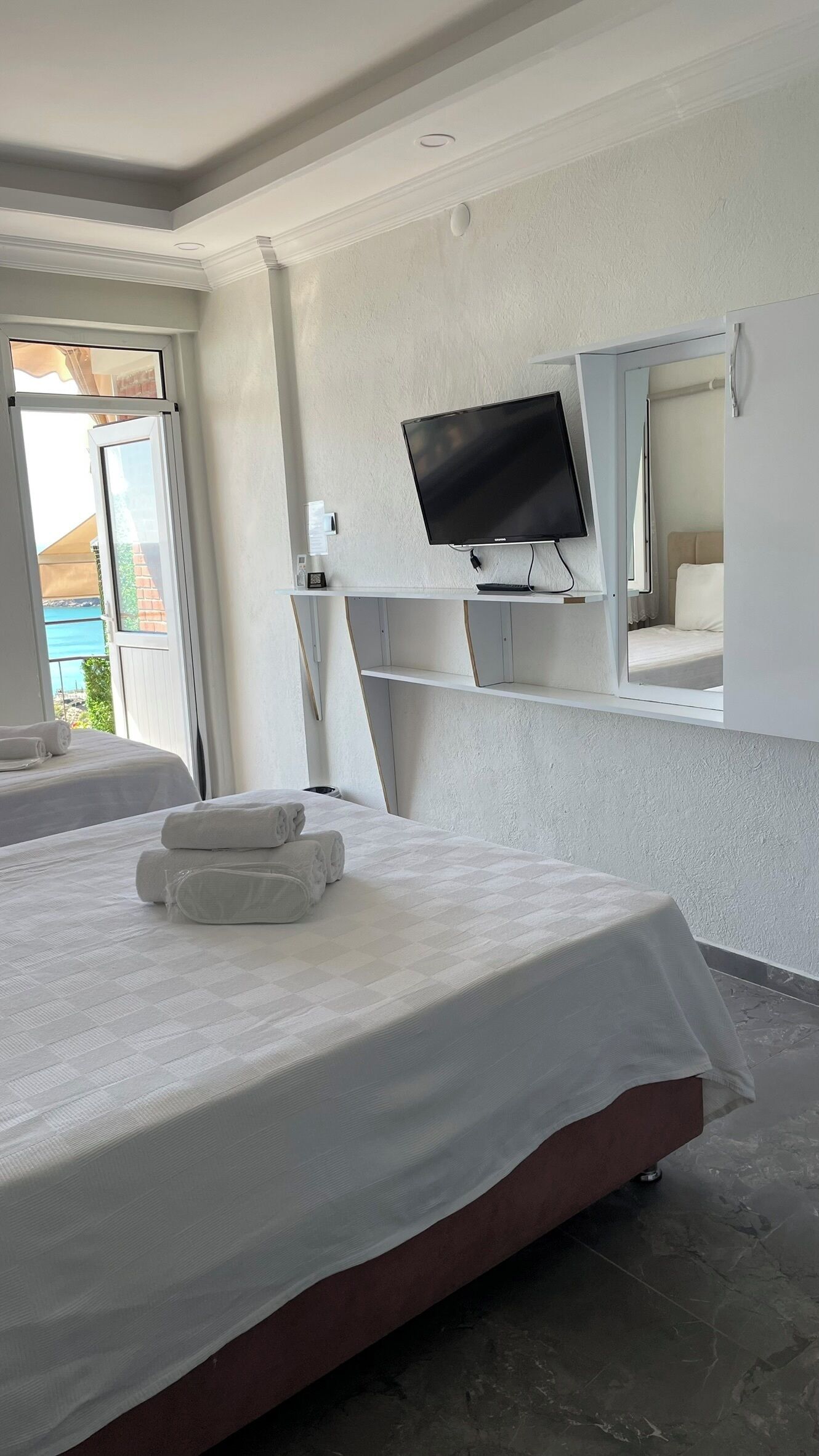 Habitación de hotel con cama, televisión montada en la pared y ventana con vista al mar.