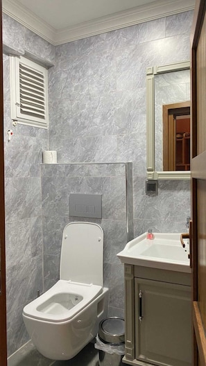 Ein Badezimmer mit Toilette, Waschbecken, Spiegel und Lüftung.