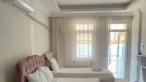 Habitación de hotel con dos camas, un ventanal con cortinas traslúcidas y un equipo de aire acondicionado instalado en el techo.