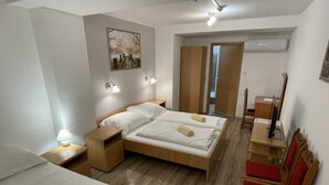 Una habitación de hotel con una cama, mesitas de noche, un escritorio con una silla, un espejo y un cuadro en la pared.