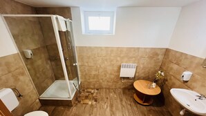 Un baño con ducha, inodoro, lavabo y un pequeño ventanal.