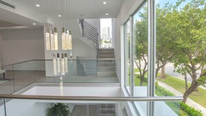 A modern interior with a glass railing, a staircase, and a view of greenery outside. - 4BR Brickell Luxury, Rooftop Pool, PingPong, City Views (Miami)
