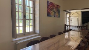 Un salón de conferencias con una mesa larga, sillas, un radiador, una ventana y un cuadro en la pared.