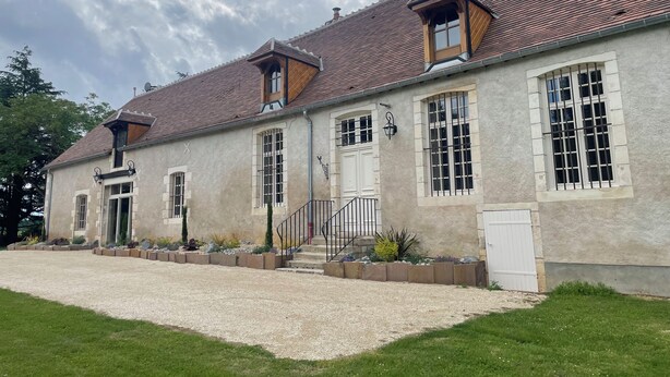 Un edificio de dos pisos con fachada de piedra, varias ventanas y un camino de entrada de grava.