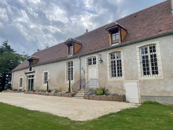 A two-story building with a stone facade, multiple windows, and a gravel driveway.