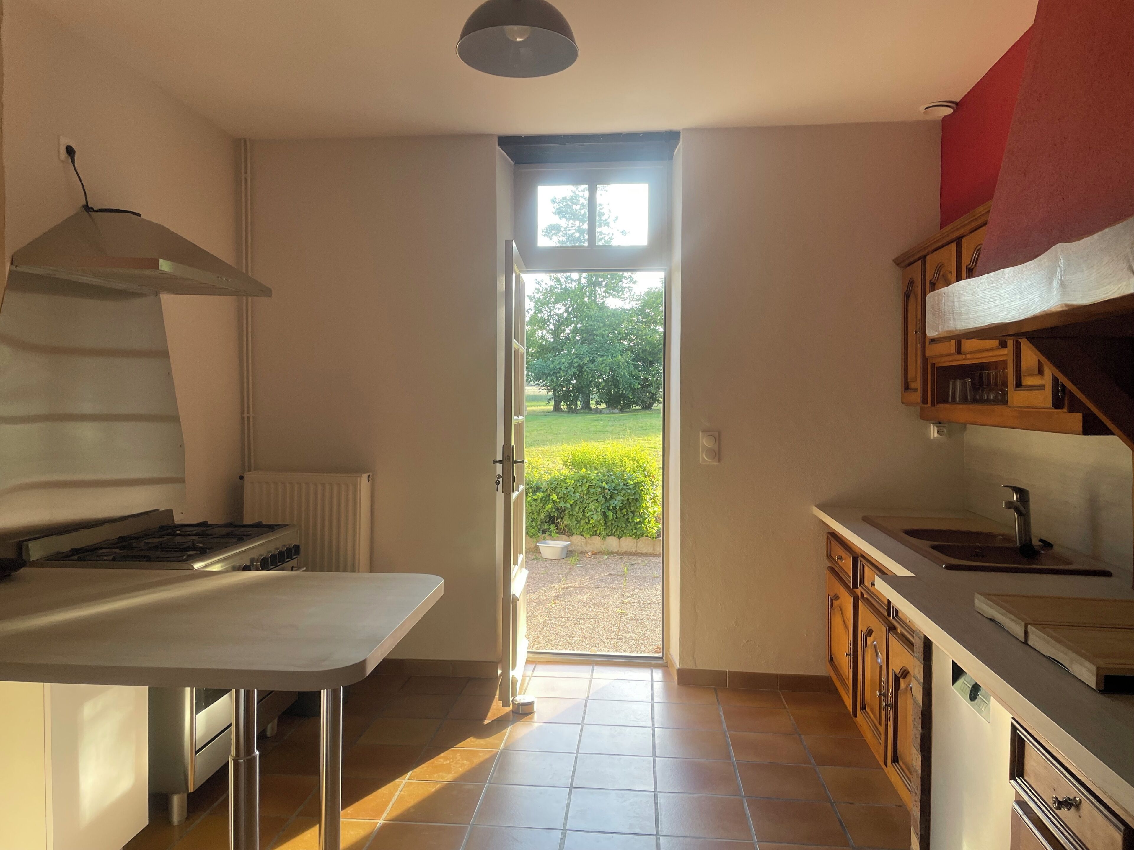 A kitchen with a stove, oven, and a view of a garden through an open door.