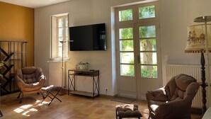 Un salón con televisor, dos sillones, una mesita y una ventana con vistas al verdor.
