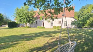 Una silla mecedora de mimbre blanco en un jardín con césped y un edificio al fondo.