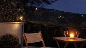 Eine Terrasse mit Tisch und Stuhl, einer Kerze und Blick auf einen Hügel mit Lichtern.