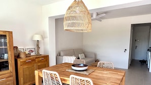 Ein Essbereich mit Holztisch, Korbstühlen, einer gewobenen Pendelleuchte, einer Couch und einem Schrank mit Glastüren.