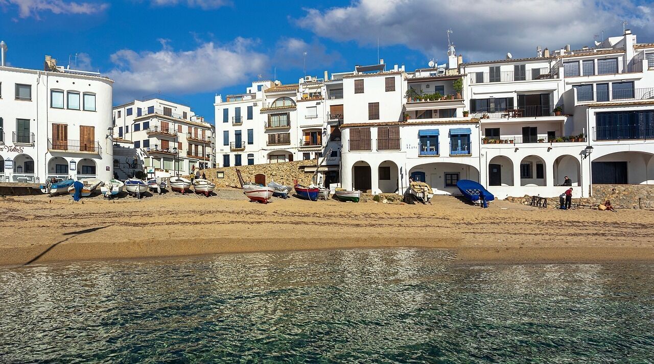 A coastal town with white buildings, a sandy beach, and boats.