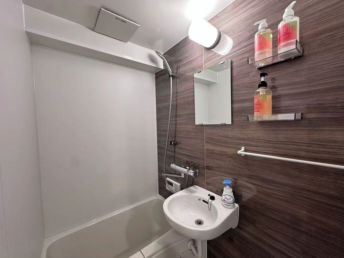 A bathroom with a shower, sink, mirror, and toiletries.