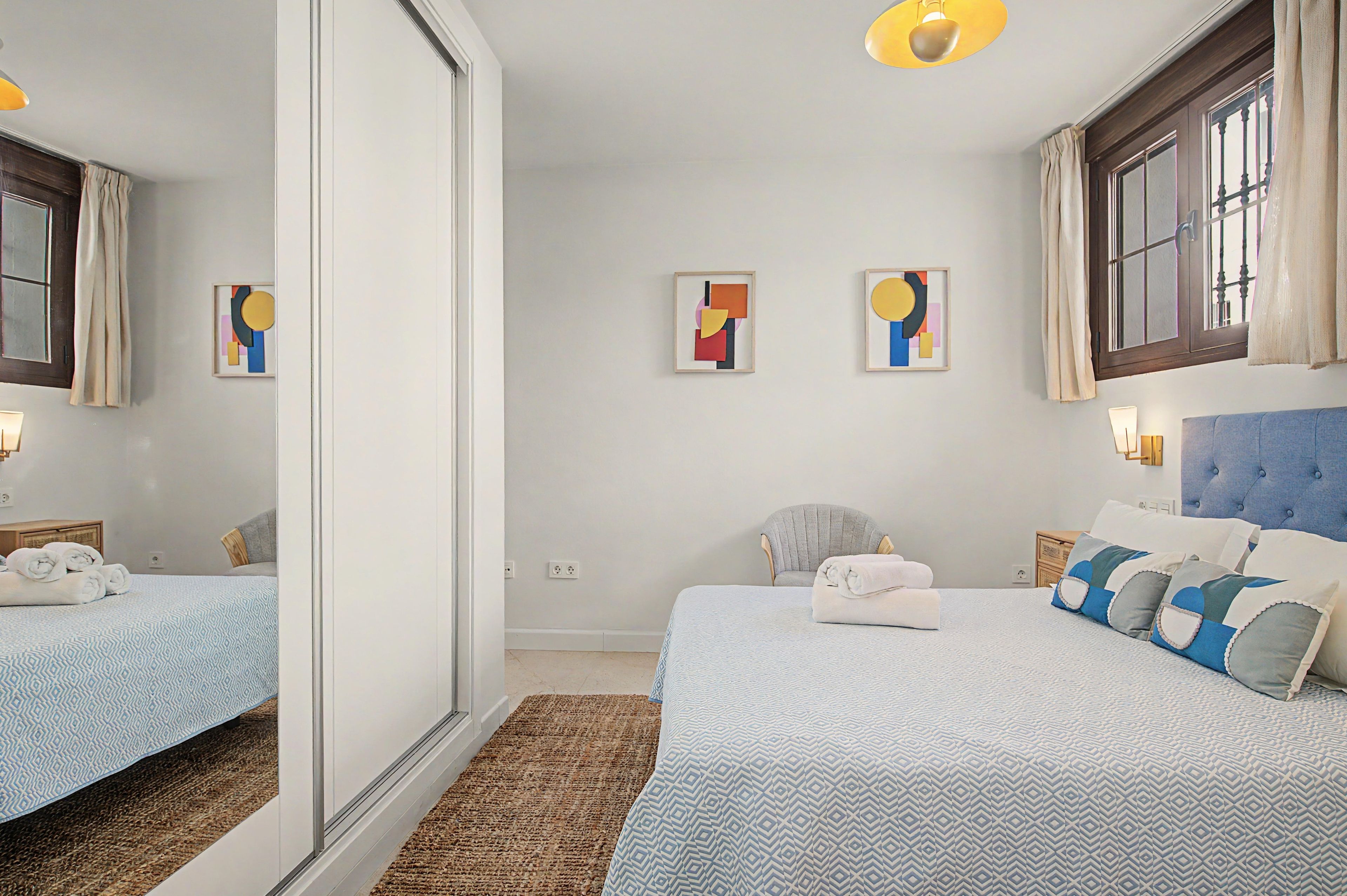 Een hotelkamer met twee bedden, een grote spiegel, kunst aan de muur en een raam met gordijnen.