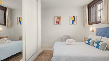 Een hotelkamer met twee bedden, een grote spiegel, kunst aan de muur en een raam met gordijnen.