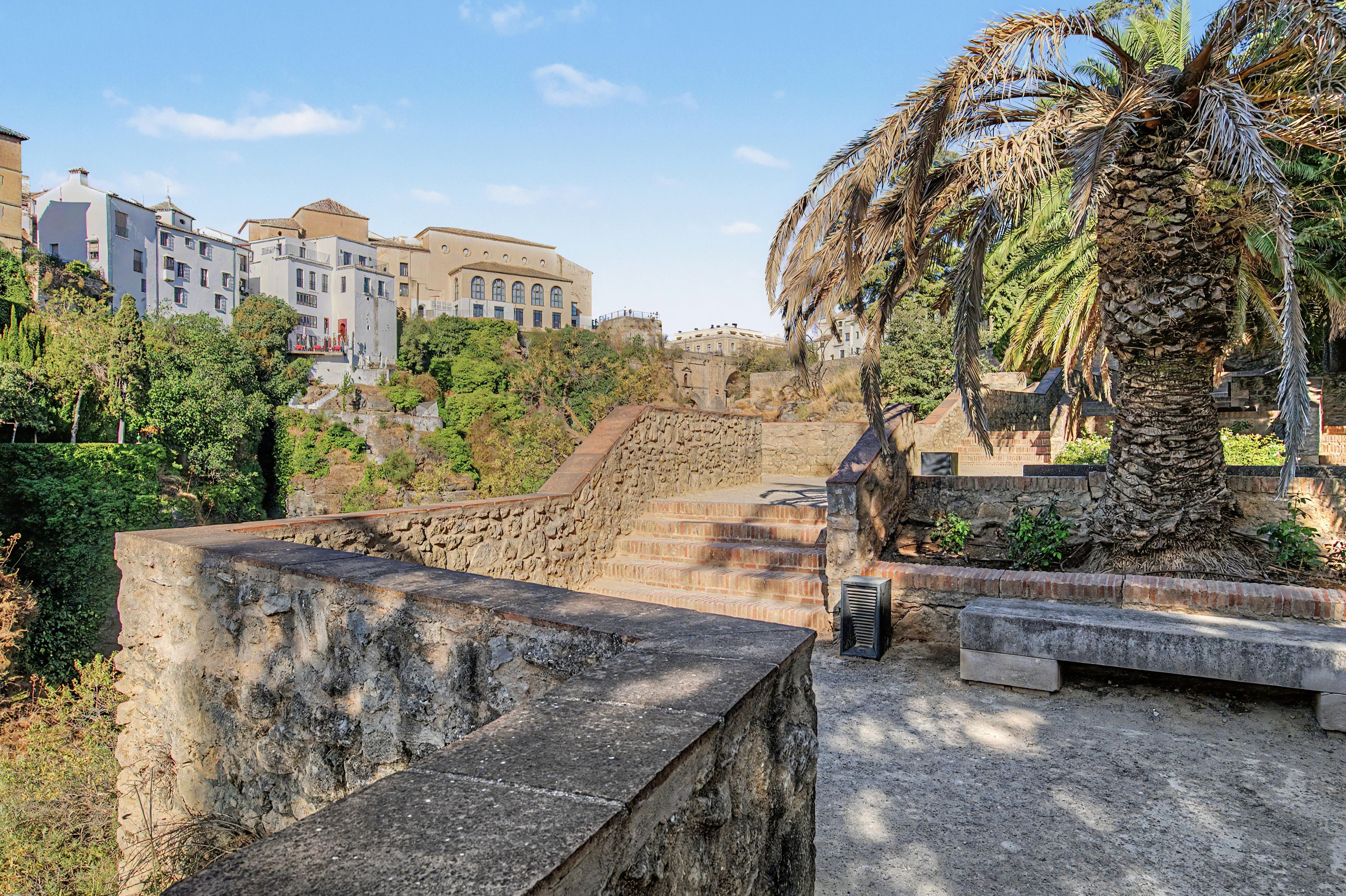 Una escalera de piedra conduce a un edificio de techo plano, rodeado de vegetación y palmeras.