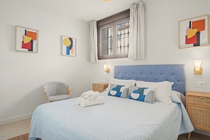 A bedroom with a blue upholstered headboard, a bed with patterned bedding, a chair, and artwork on the walls. - Apartment 'La Mina' with Terrace, Wi-Fi and Air Conditioning (Ronda)