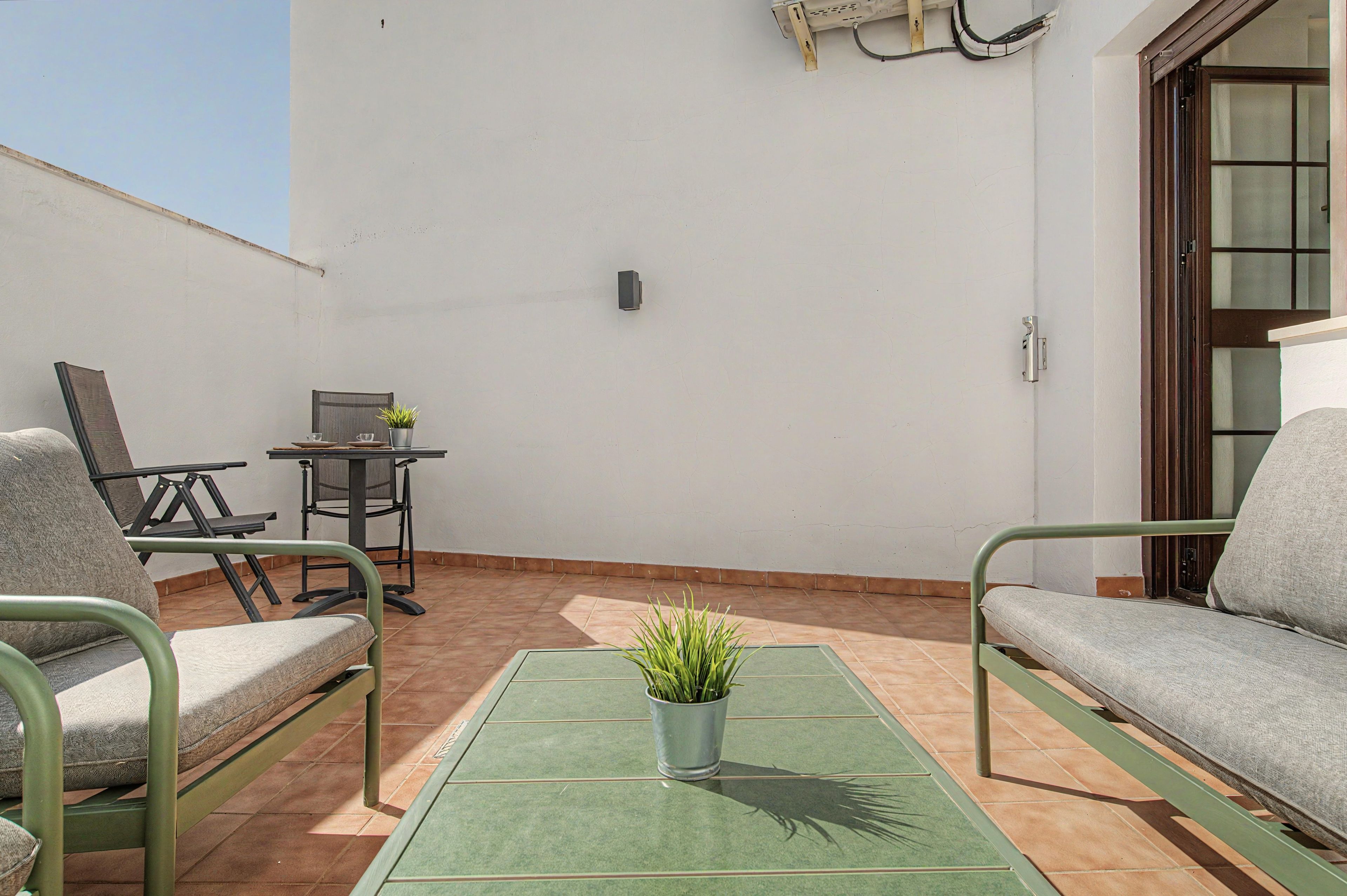 A patio with a table, chairs, a small table with a plant, and a door.