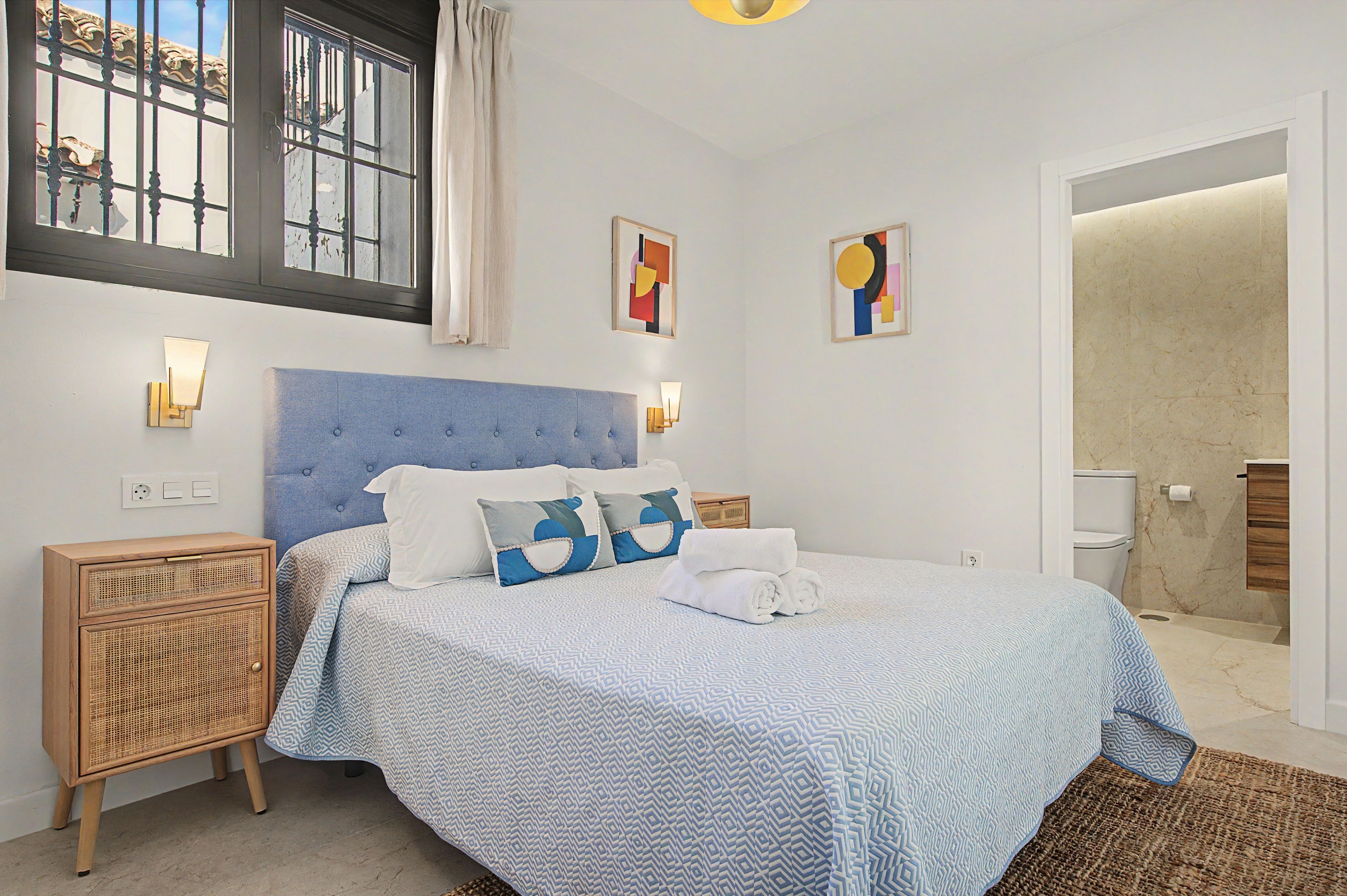 Ein Schlafzimmer mit Bett, Nachttischen, Wandbildern und Blick ins Freie.