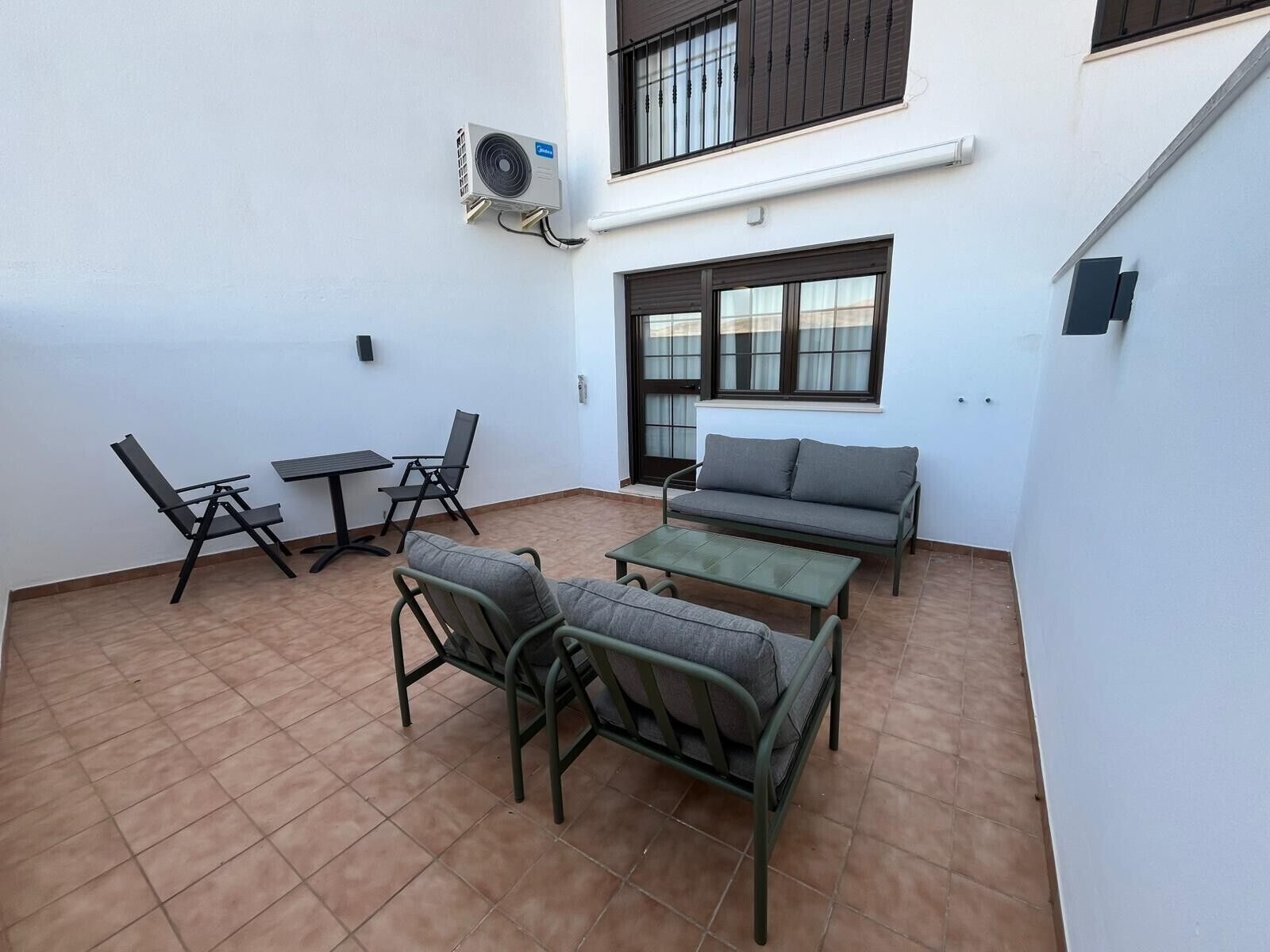 Eine Terrasse mit Tisch, Stühlen, einer Couch und einer Klimaanlage.