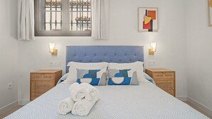 A bedroom with a bed, two bedside tables, a window with curtains, and a wall-mounted artwork.