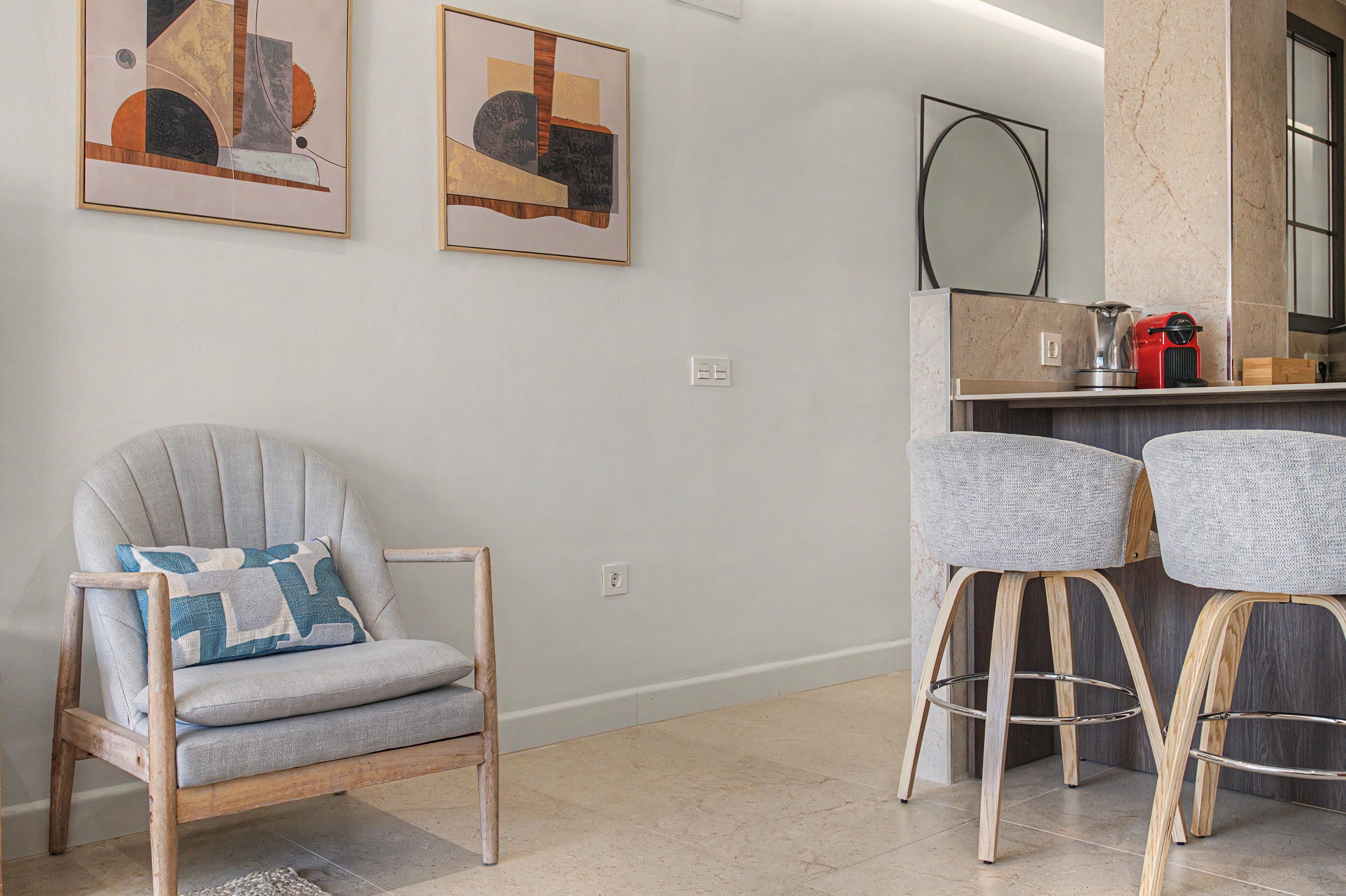 Uma sala de estar moderna com uma poltrona cinza, dois bancos altos e uma obra de arte abstrata na parede.