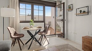 A modern dining area with a round table, two chairs, a floor lamp, and a view through a large window.