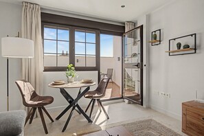 A modern dining area with a round table, two chairs, a floor lamp, and a view through a large window.