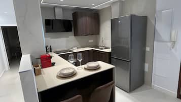 Eine moderne Küche mit Kochinsel, dunklen Holzschränken, einem Edelstahl-Kühlschrank und einer eingebauten Mikrowelle.