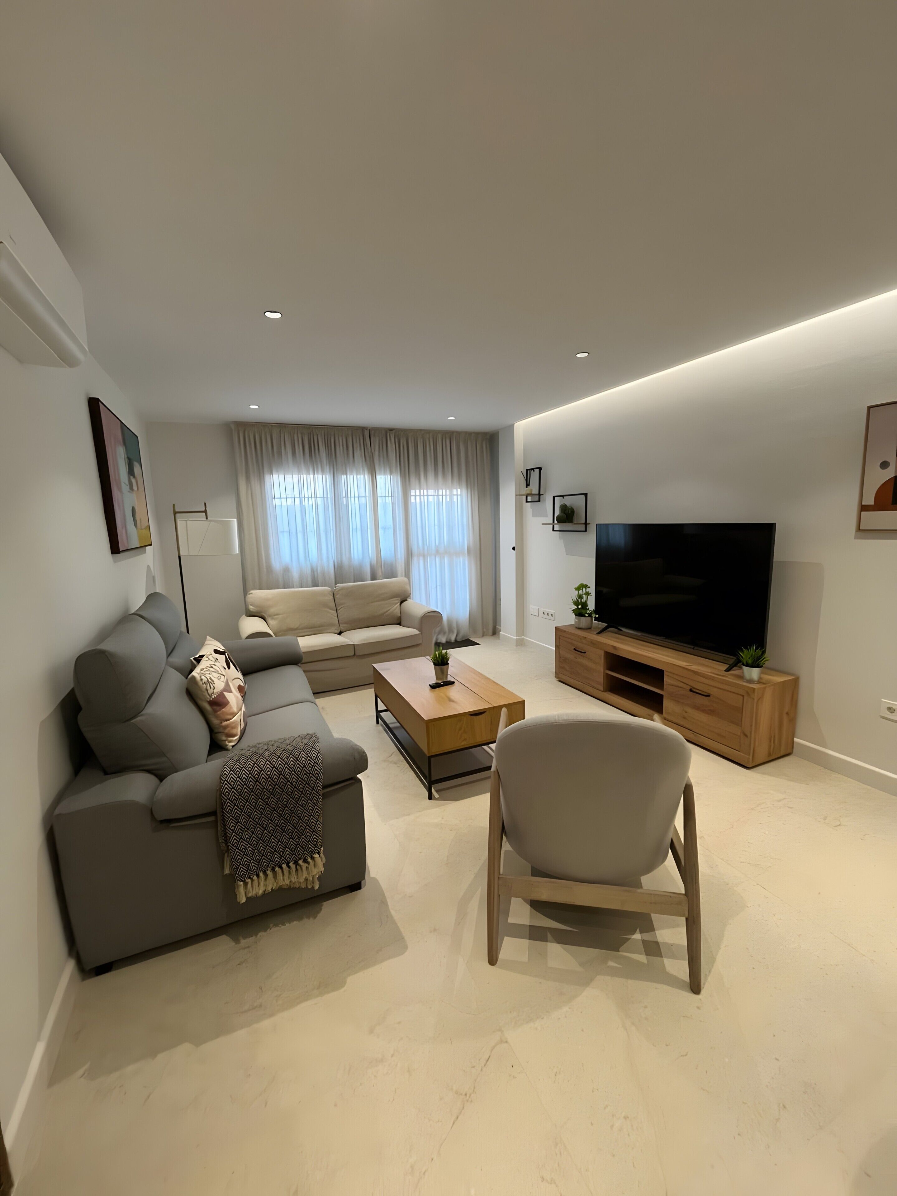 Ein modernes Wohnzimmer mit einer Couch, einem Couchtisch, einem Fernseher und einem Sessel.