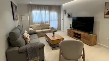 Ein modernes Wohnzimmer mit einer Couch, einem Couchtisch, einem Fernseher und einem Sessel.