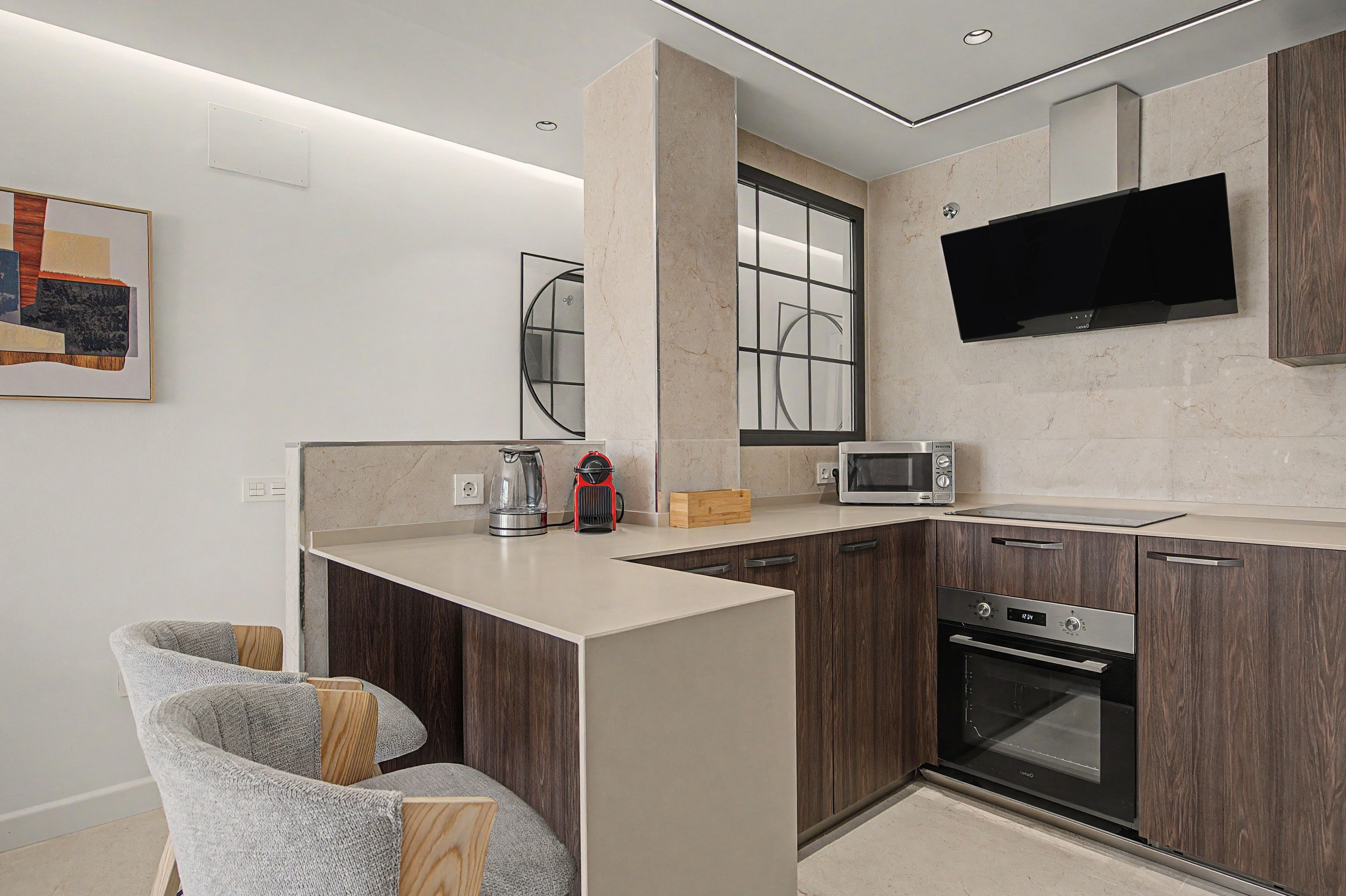 A modern kitchen with a built-in oven, microwave, and a large flat-screen TV mounted above the counter.