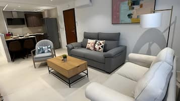 Ein modernes Wohnzimmer mit grauem Sofa, einem weißen Sessel, einem Holztisch und einer grauen Couch.