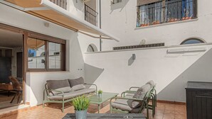 A sunlit patio with a sofa, chairs, a small table, and a potted plant.