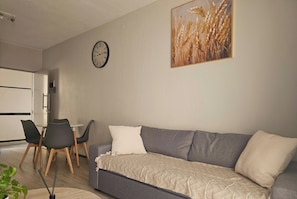 A living room with a grey sofa, a clock, and a painting of wheat on the wall. - 1st Generation Style (Johannesburg)
