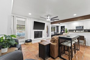 Una sala de estar moderna con chimenea, comedor y cocina con armarios blancos y encimera negra.